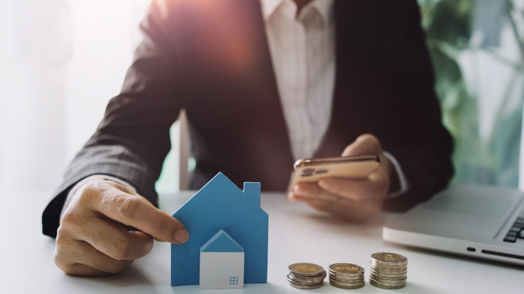 Man Holding House on Table with Pound Coins and Phone 