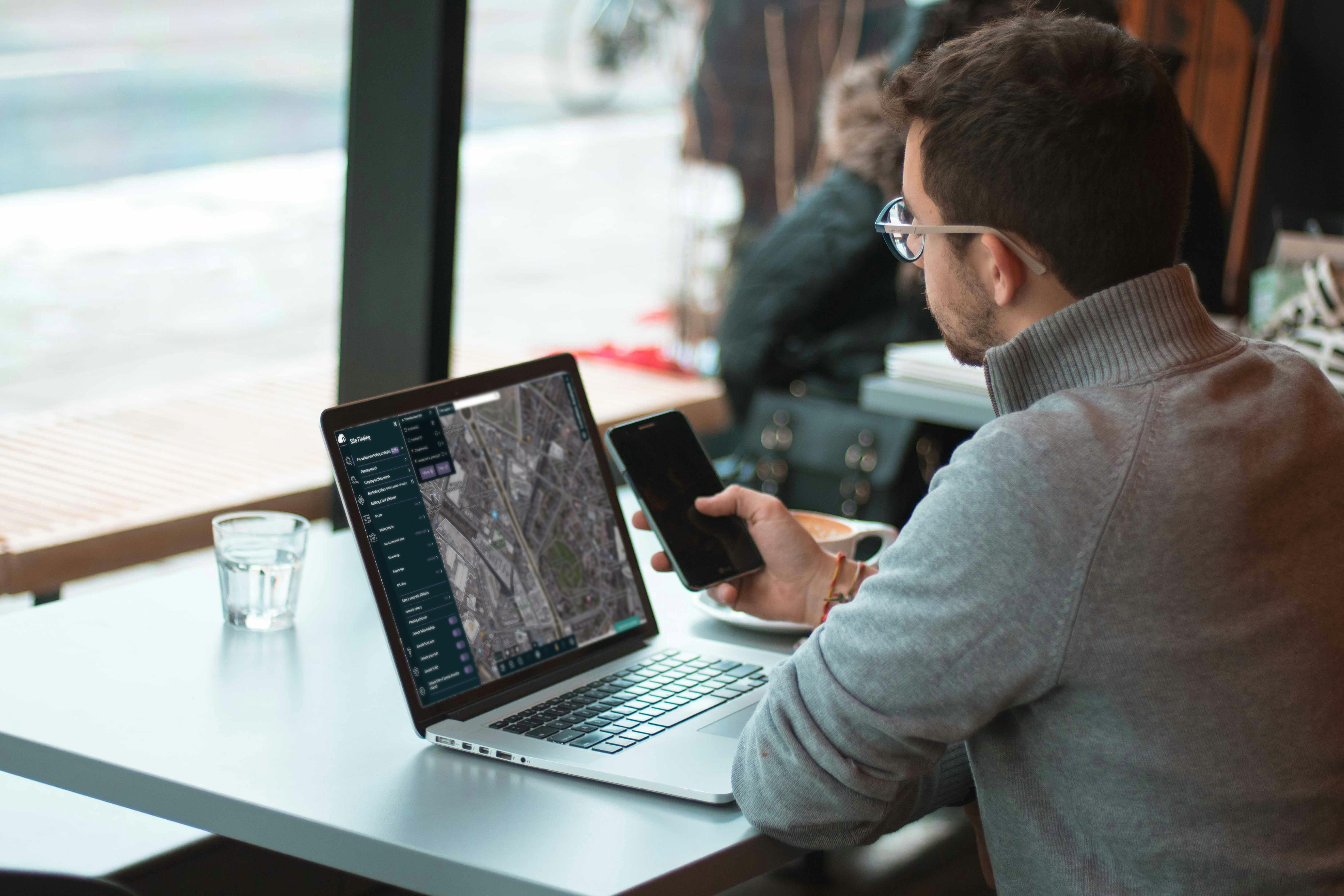 Nimbus_Man on Laptop holding phone in coffee shop_Mockup
